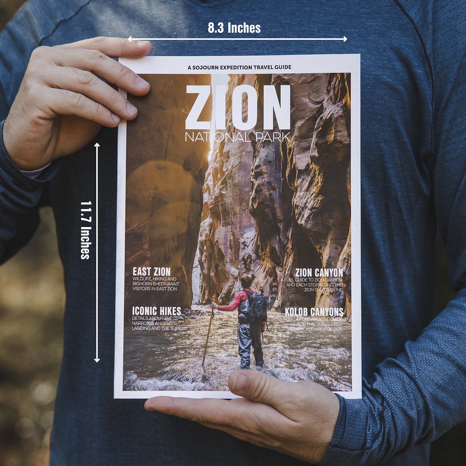 Person holding a travel guide for Zion National Park with dimensions displayed.